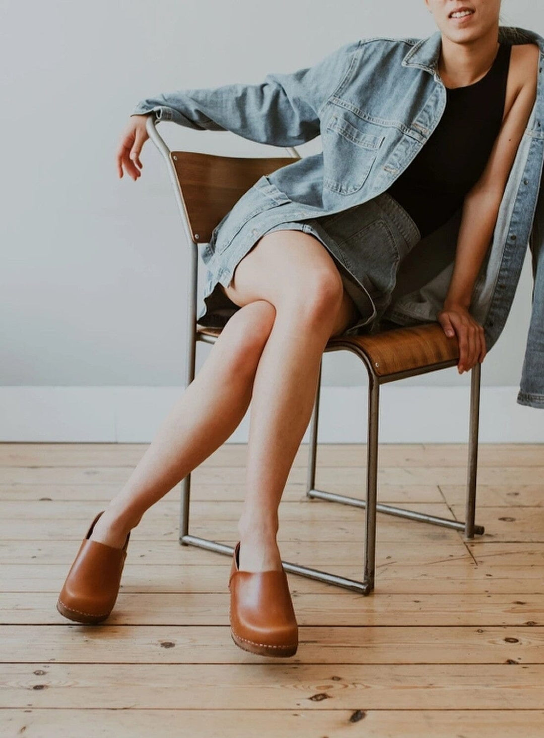 Low Jord Clog by KIT + CLOGS worn by a model on a chair wearing a light denim skirt and jacket with a black strap top